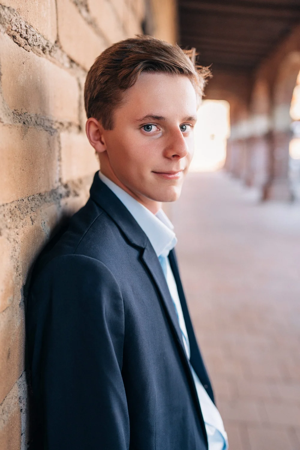 Christian leaning against a stone wall in the mission corridor, looking off, Mission San Juan Capistrano senior session