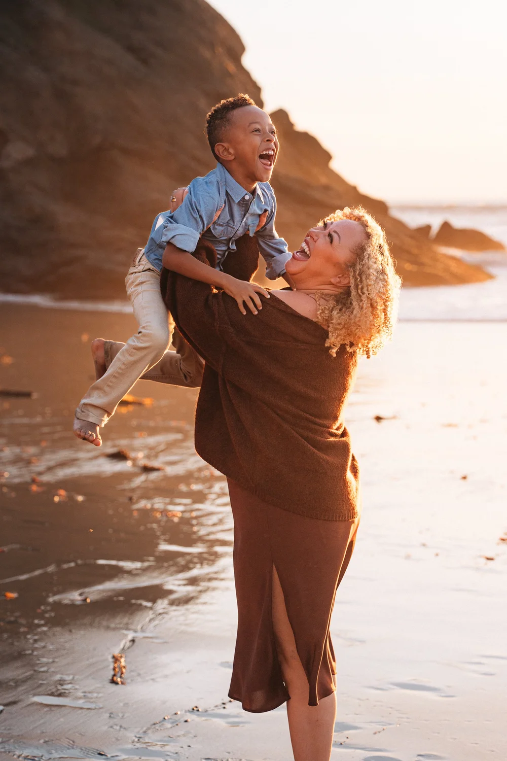 Mom lifting her son into the sunset, both mid-laugh