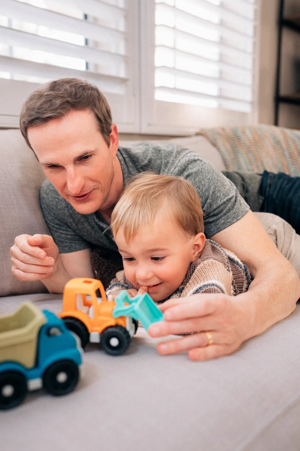 Dad and toddler playing with toy trucks on the couch