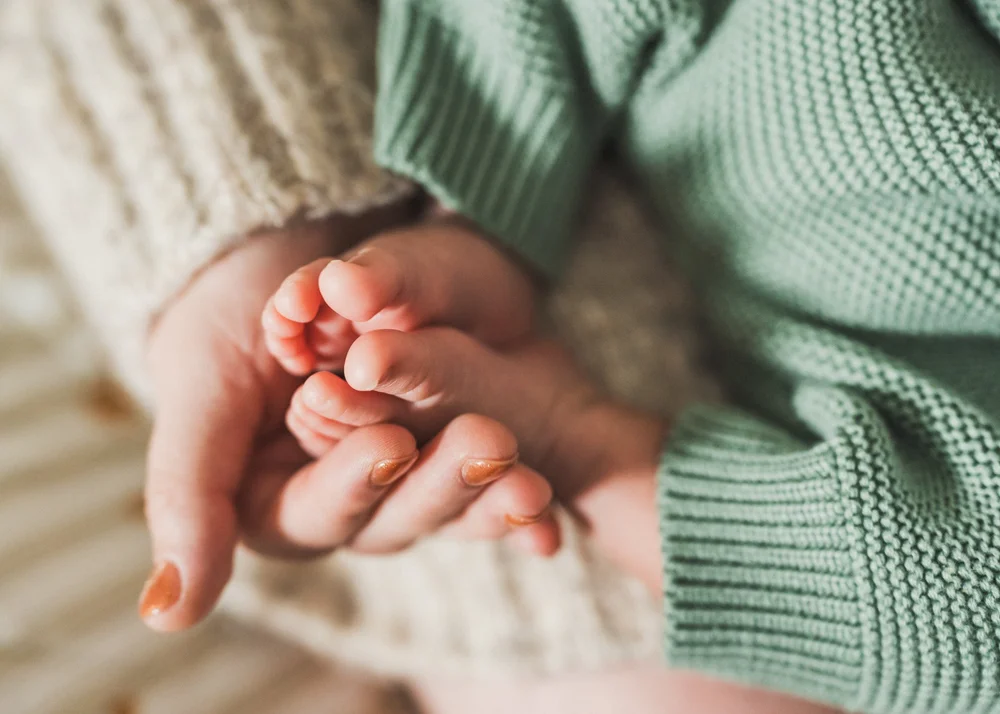 Tiny newborn feet cradled in mom's hand against a green knit sleeper, Nathan and Ana in-home session San Diego