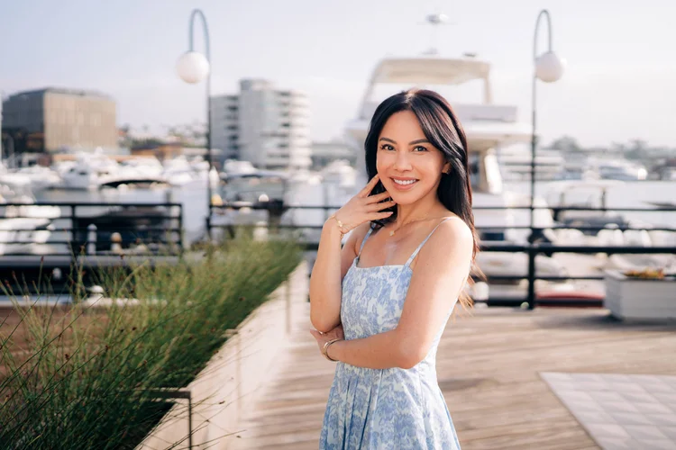 A woman in a blue floral dress smiling on the boardwalk beside the marina at Lido Marina Village