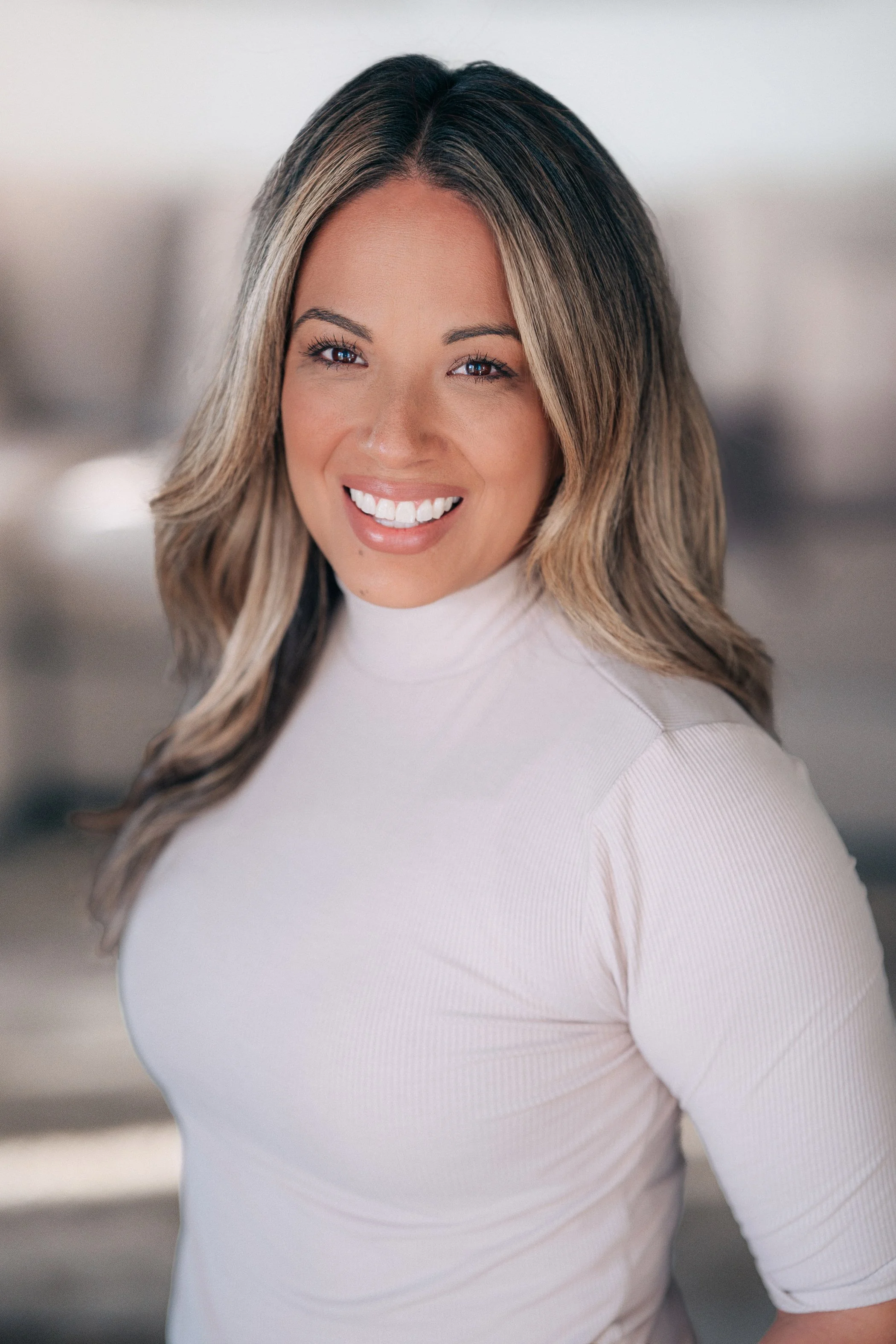 A woman with shoulder-length wavy hair smiling wearing a white top.