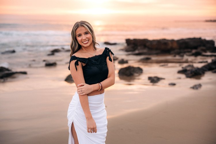 A young woman smiling on the beach at sunset during a senior session at Crystal Cove