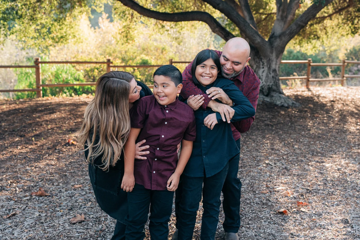 A family of four laughing together beside the rustic fence at Carbon Canyon Regional Park