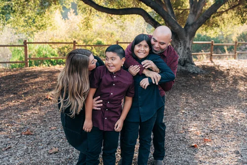 A family of four laughing together beside the rustic fence at Carbon Canyon Regional Park