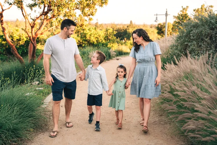 A family of five holding hands and laughing on a golden hour path at Citrus Ranch Park in Tustin