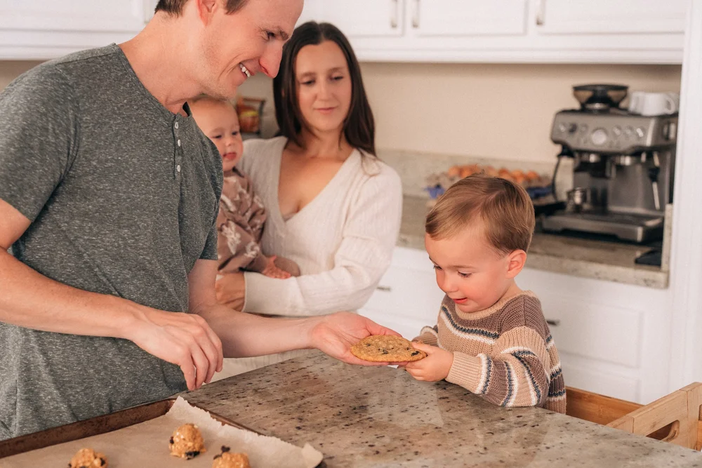 Dad handing their toddler a finished cookie across the counter