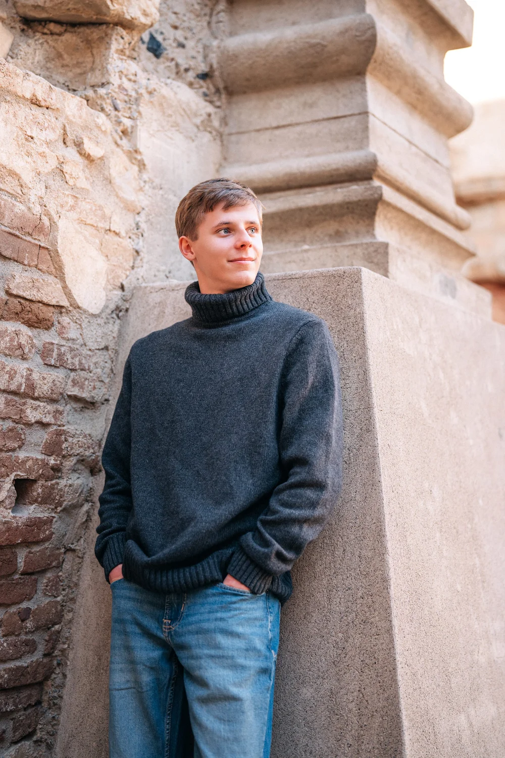 Christian in a charcoal turtleneck leaning against weathered stone columns at Mission San Juan Capistrano