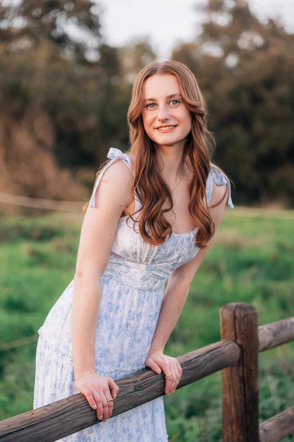 Close portrait of Emily smiling and leaning on a wooden fence at sunset, Coto de Caza senior session