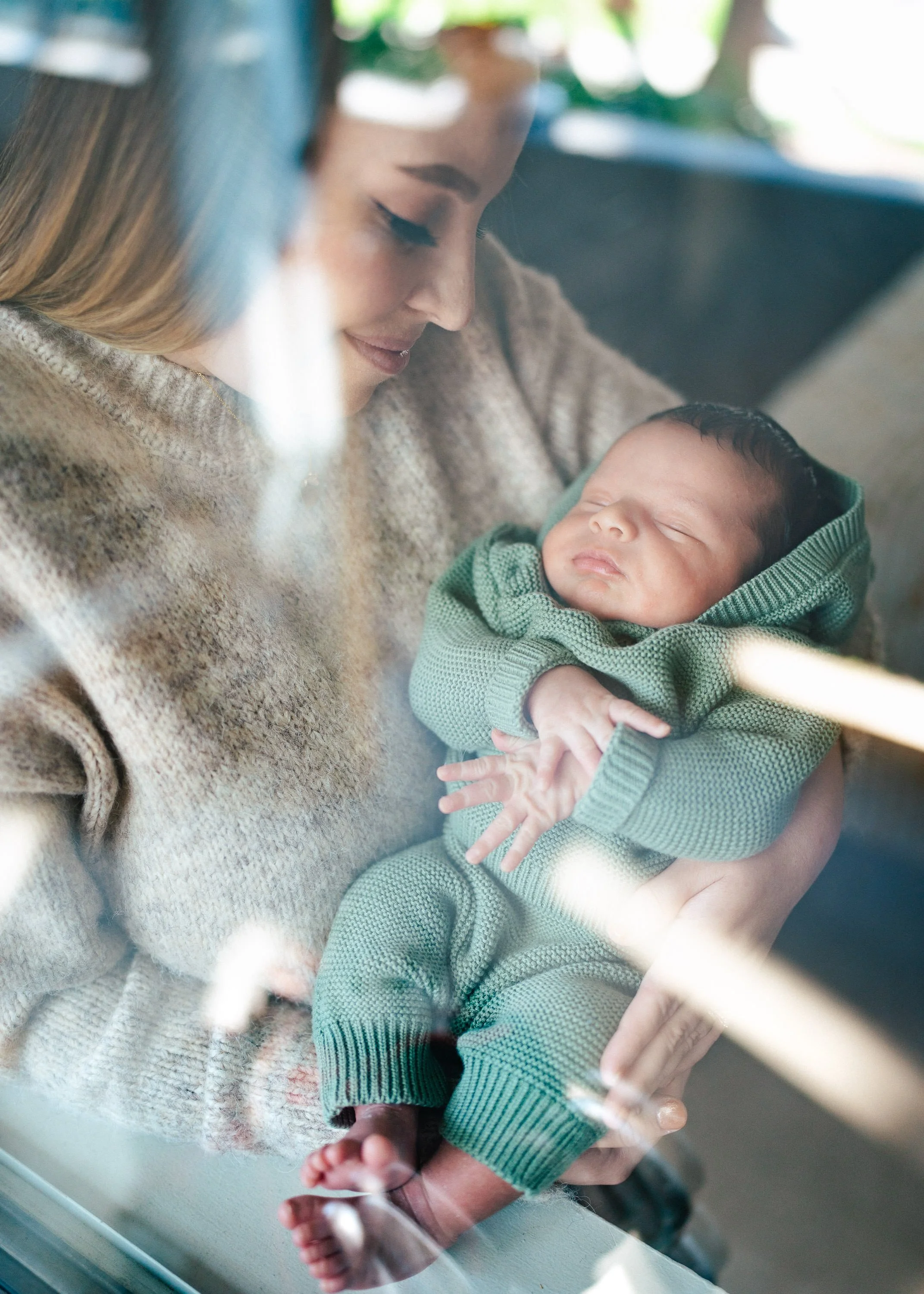A woman holding a sleeping baby dressed in a green sweater.