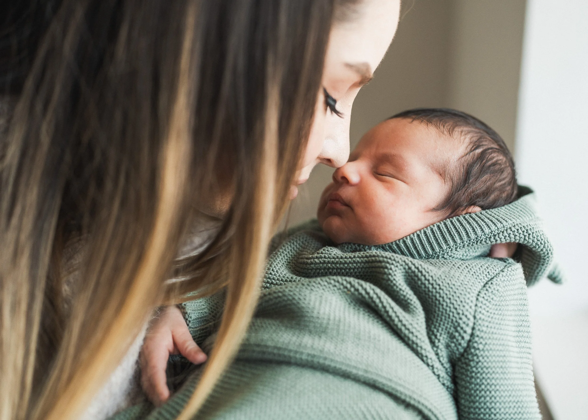 A woman holding a newborn baby close, touching foreheads, both with eyes closed, in a tender moment.