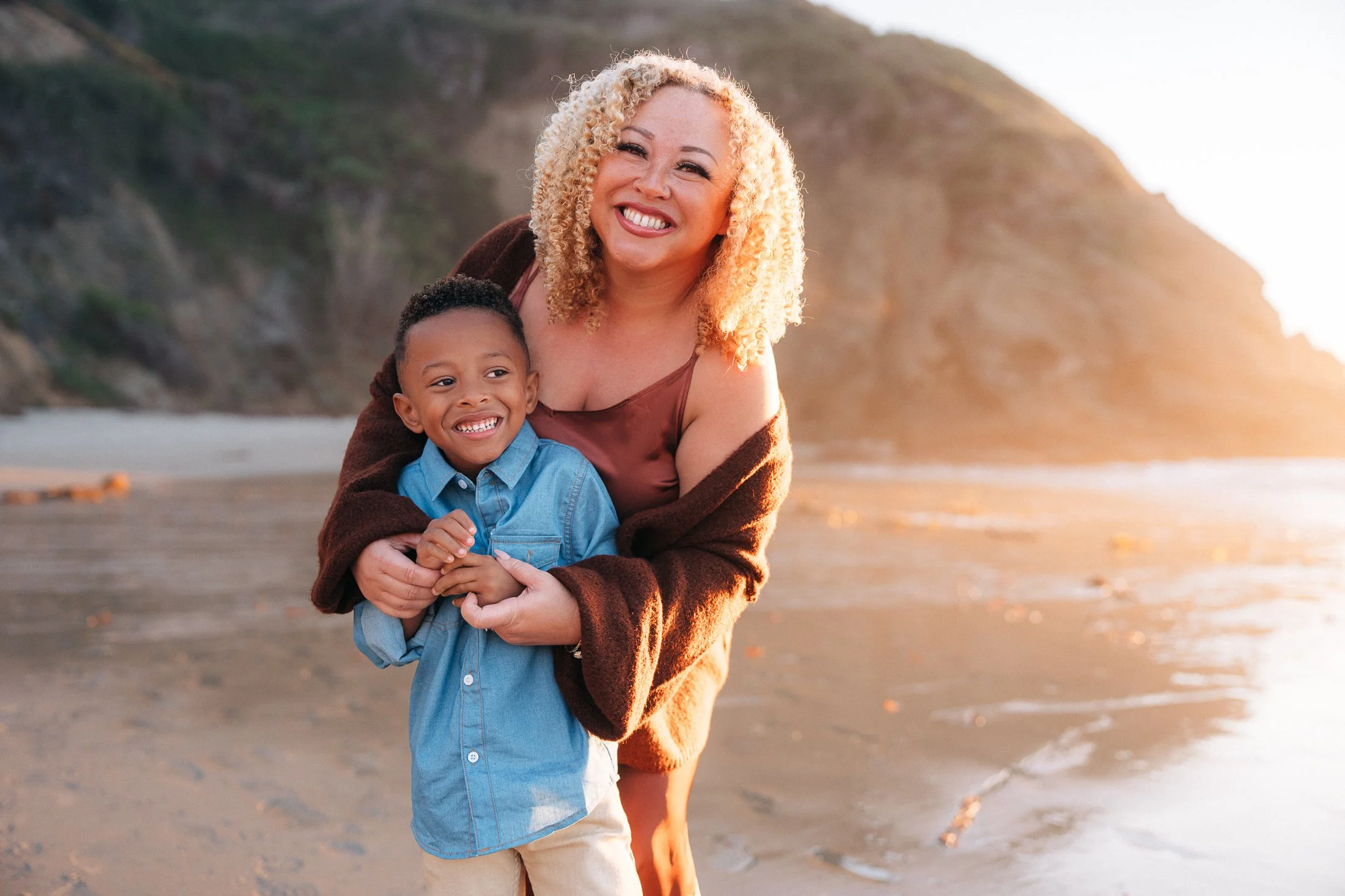 Mom hugging son from behind, both grinning in the golden light