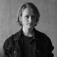 Black and white portrait of a woman with shoulder-length hair wearing a dark denim jacket, looking at the camera