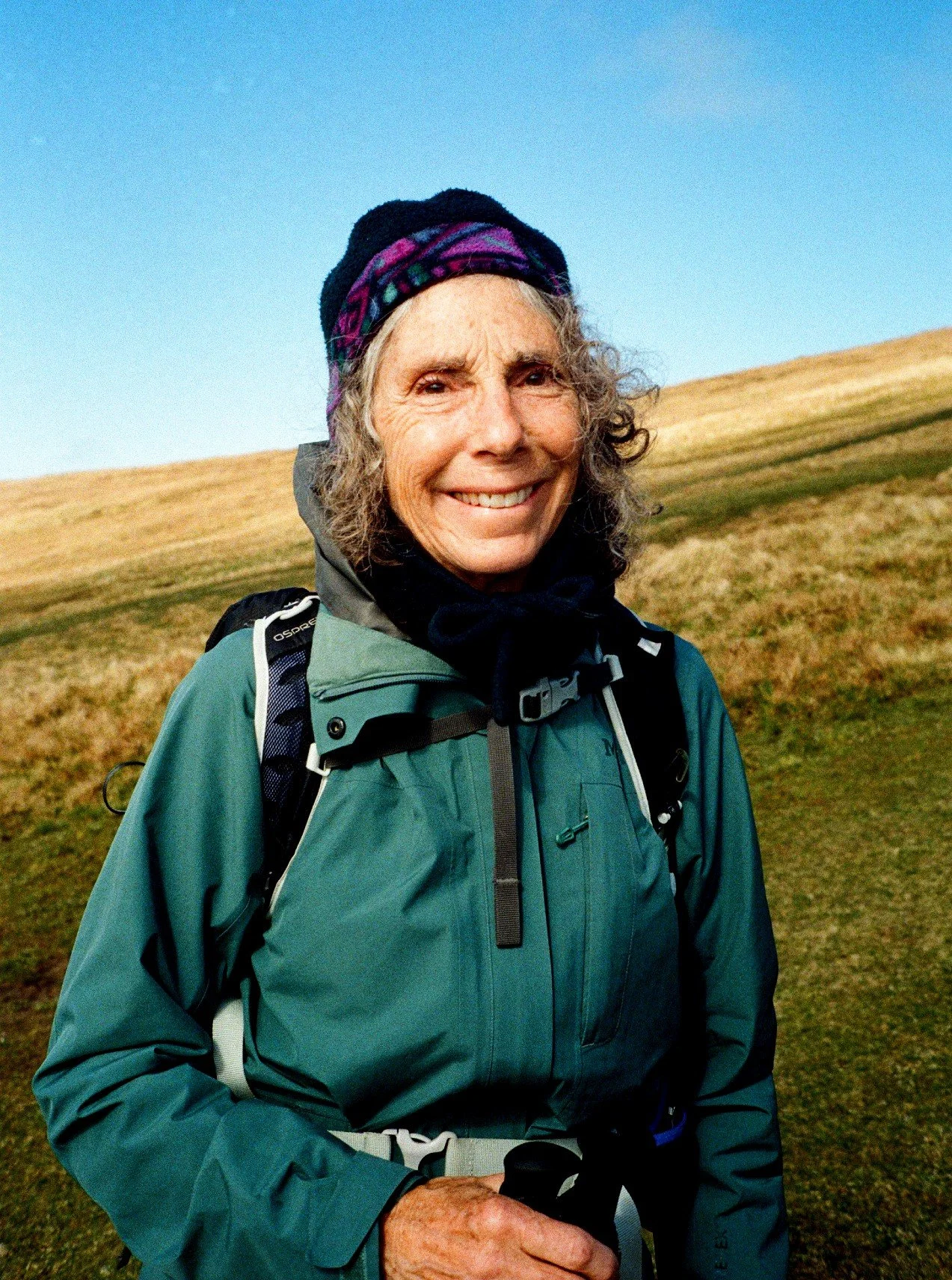 A woman who wears a turquoise Patagonia raincoat smiles at the camera. 35mm film photography in Scotland.