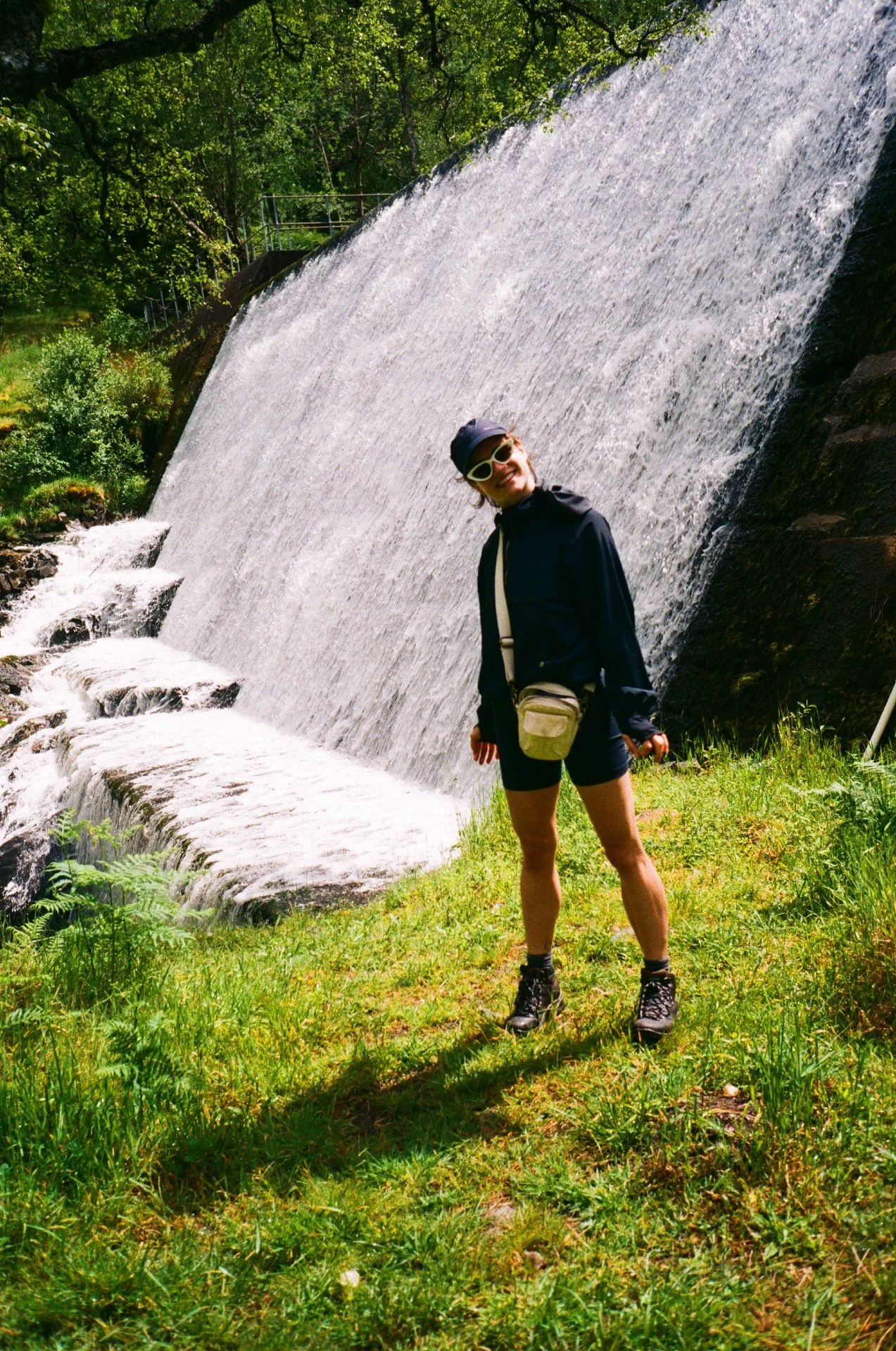 A 35mm film portrait of a woman wearing hiking gear standing near a waterfall in the Scottish Highlands. Mountain leader and outdoor instructing services available.