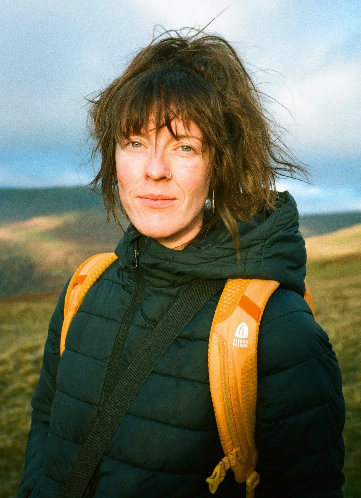35 film photograph of a woman hiking in the lake District. She is wearing a Finisterre coat and a yellow Sierra Designs rucksack.