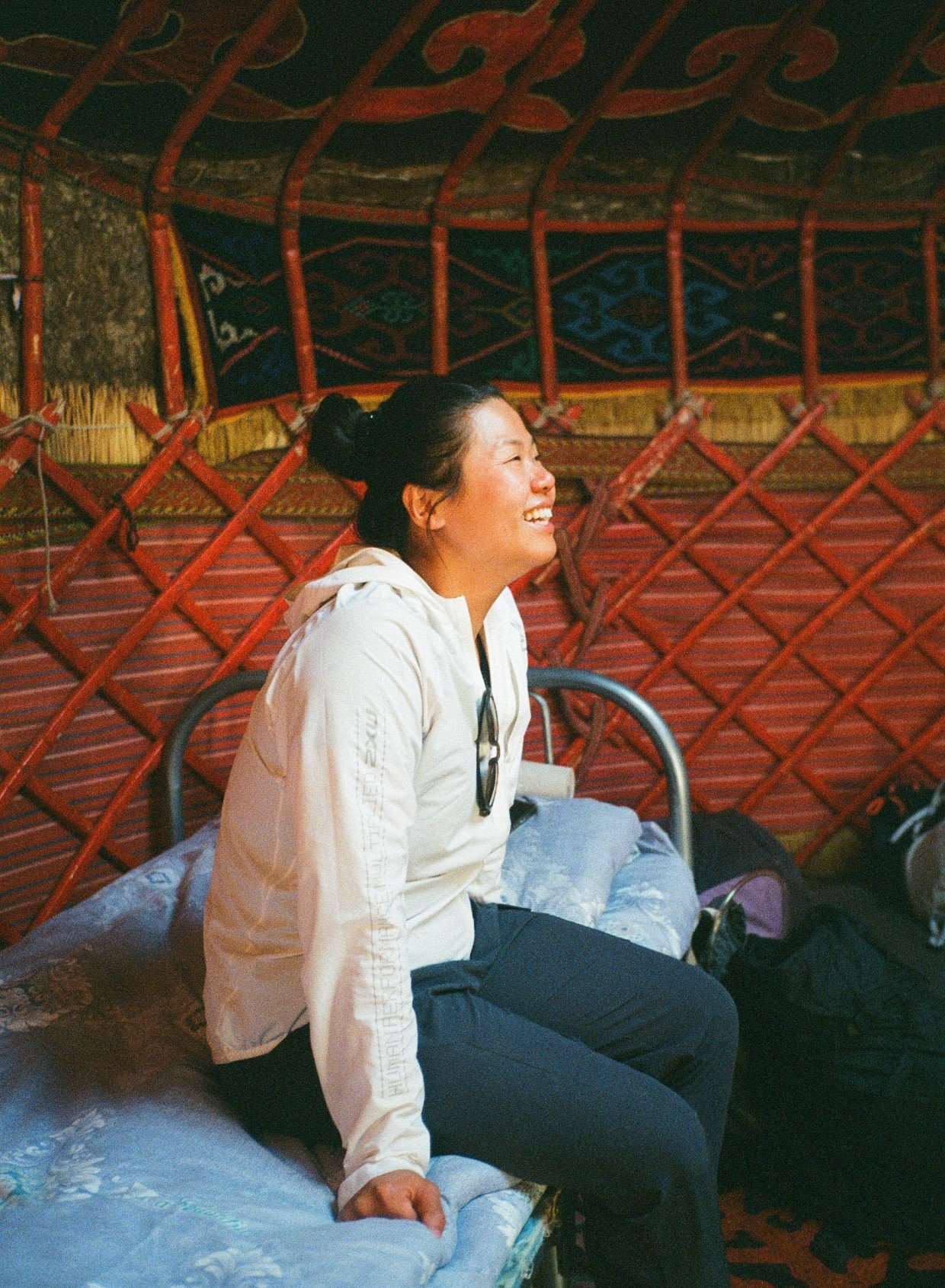 A woman dressed in hiking clothing is sat smiling on a bed inside a yurt in Tajikistan, Central Asia.