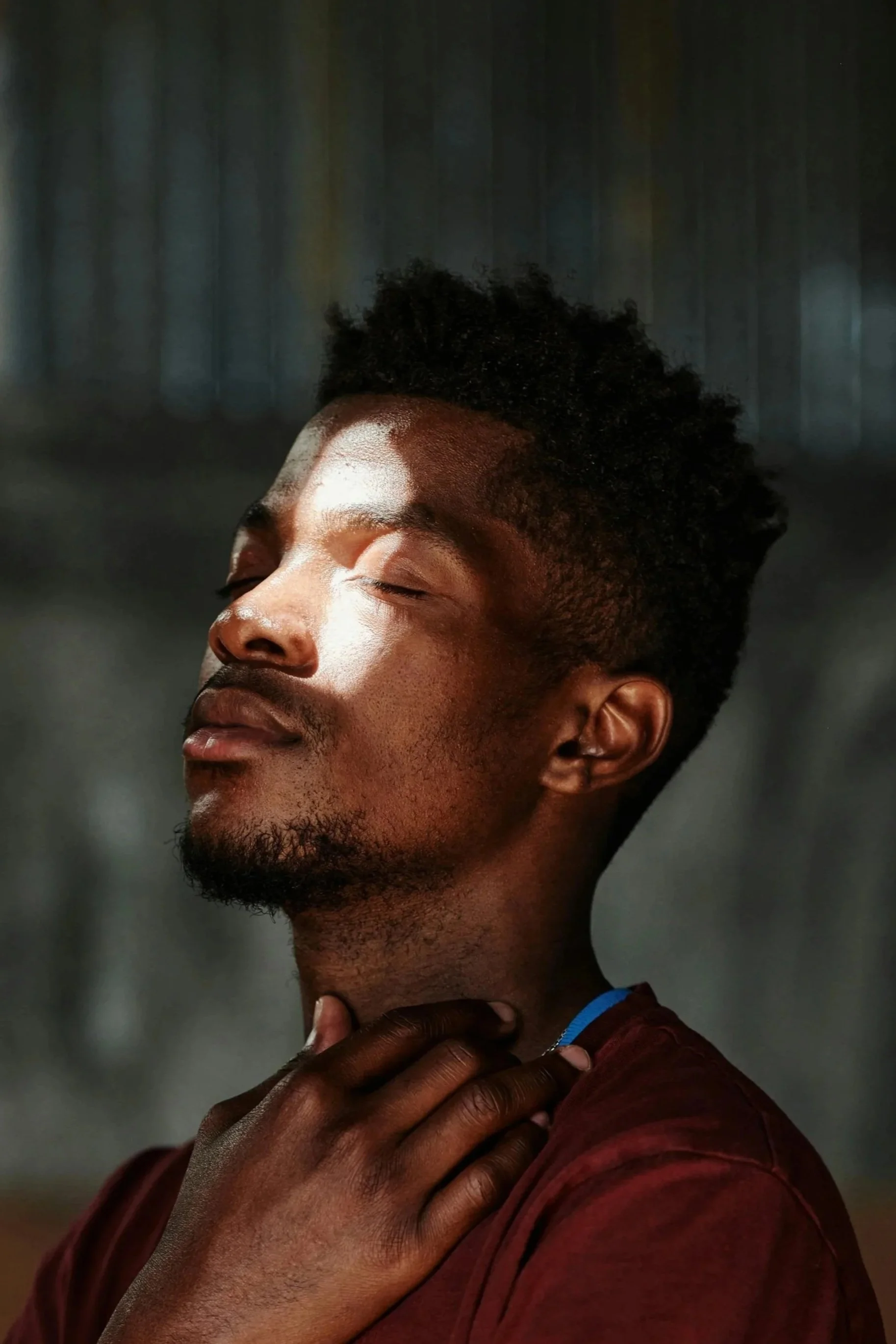 A young man with closed eyes and a peaceful expression, breathing in with eyes closed in a serene setting.