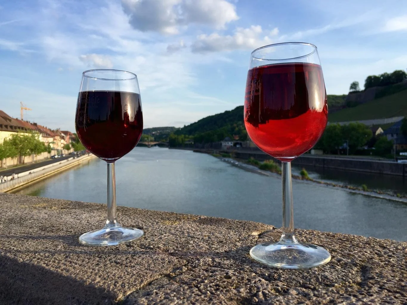 Two glasses of red wine on a wall next to a river