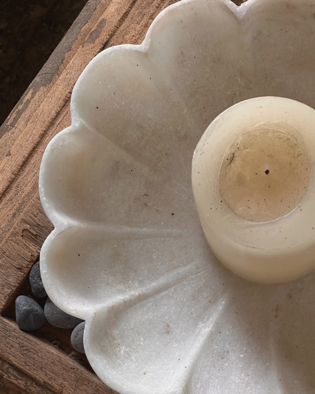 A white ceramic candle holder shaped like a flower, placed on a wooden surface with a few small black stones underneath.