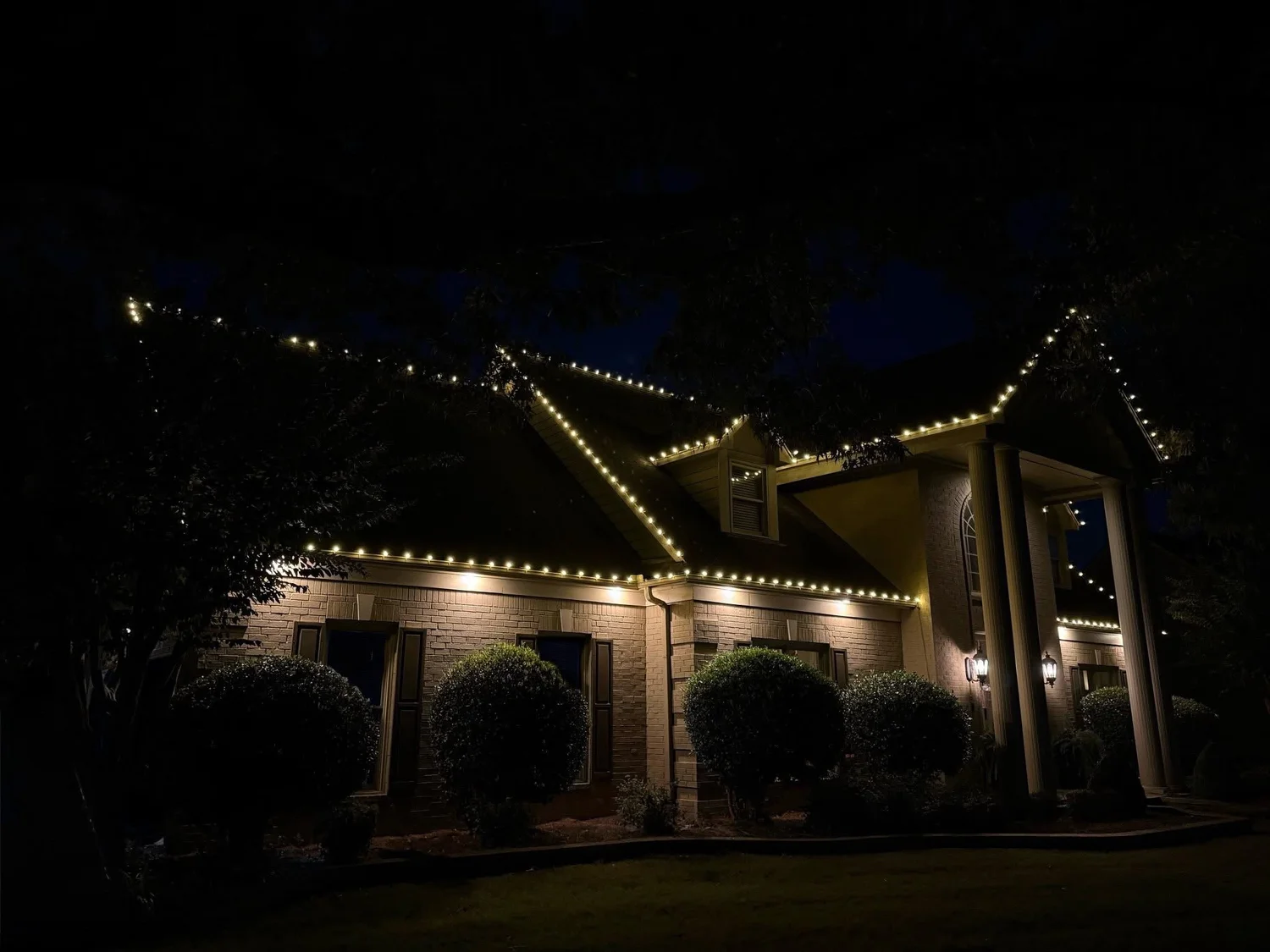 Permanent holiday lighting outlining a brick home's rooflines after dark