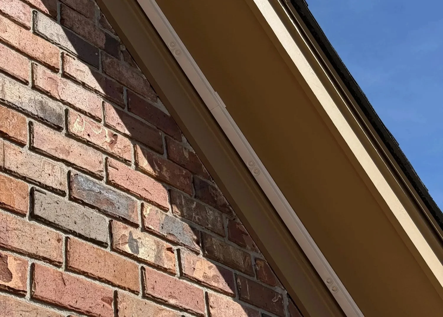 Close-up of low-profile permanent lighting track under a brick home's eave