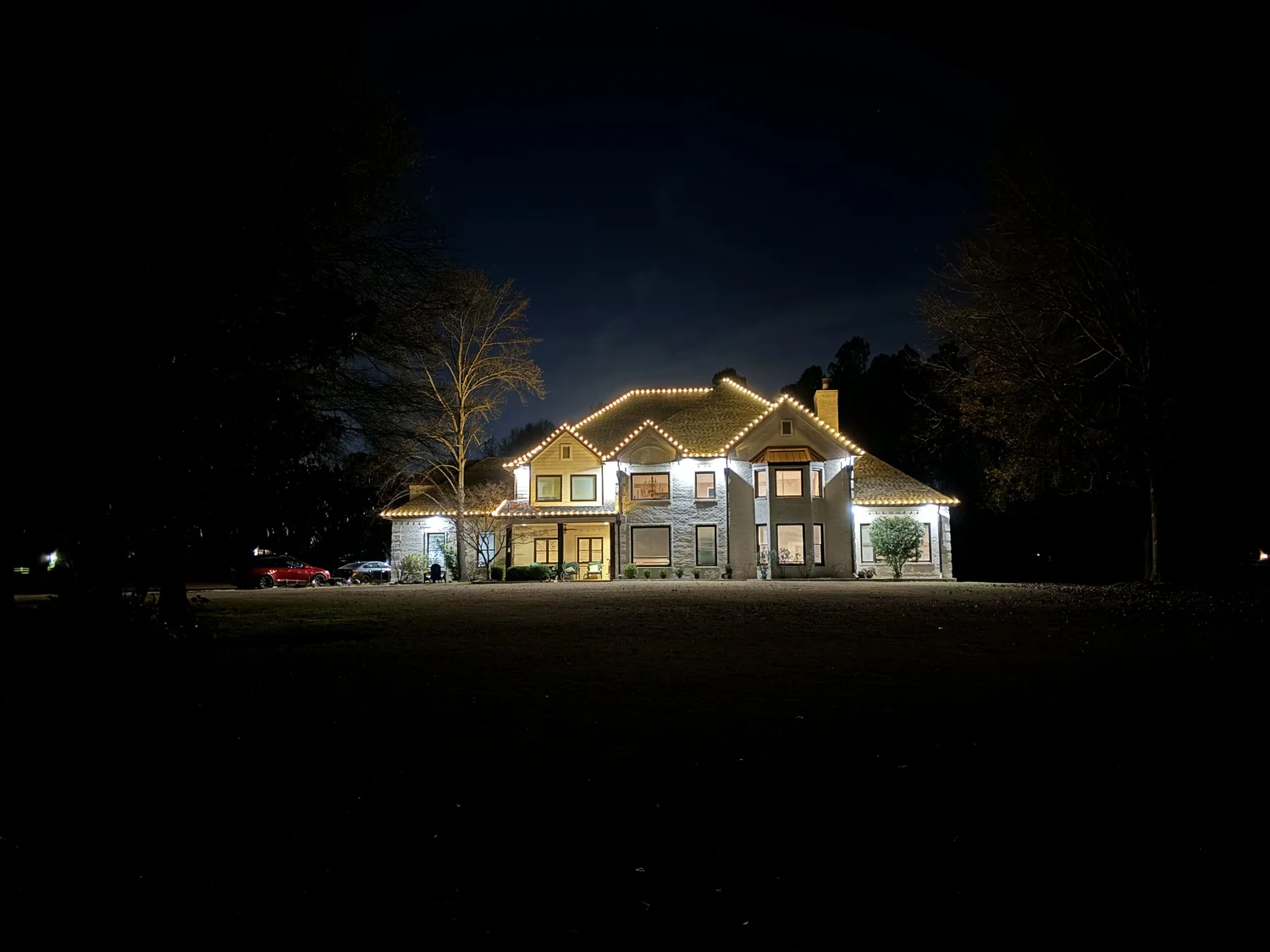Large home glowing with holiday lights at the end of a long lawn