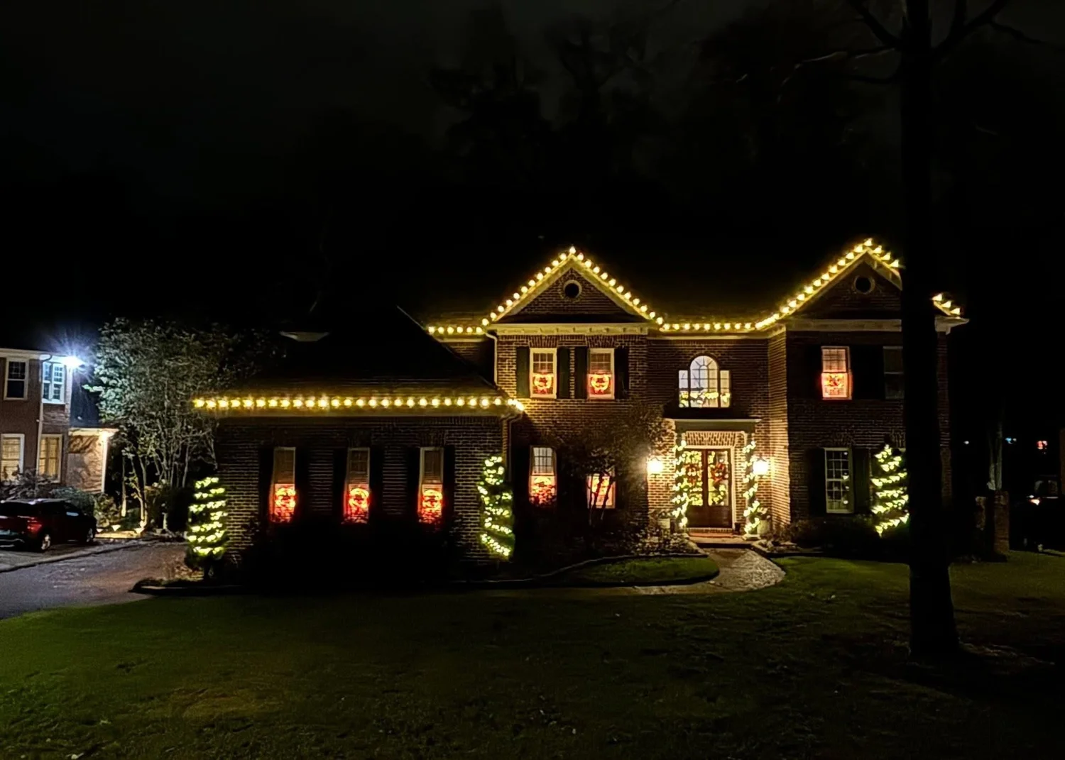 Christmas light installation with roofline lights and wrapped shrubs at night