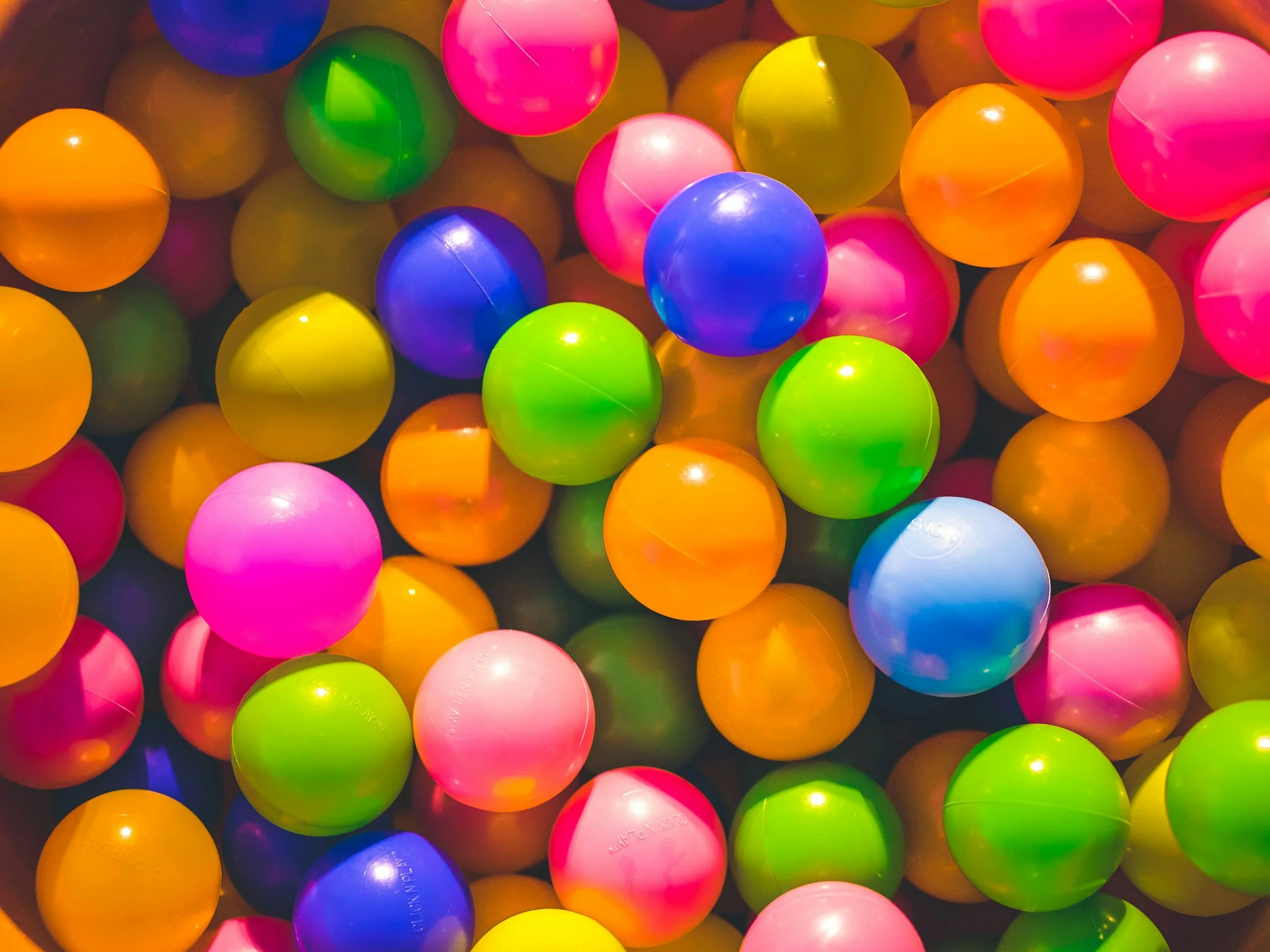 Colorful plastic balls of various bright colors including pink, orange, green, blue, and purple, piled together.