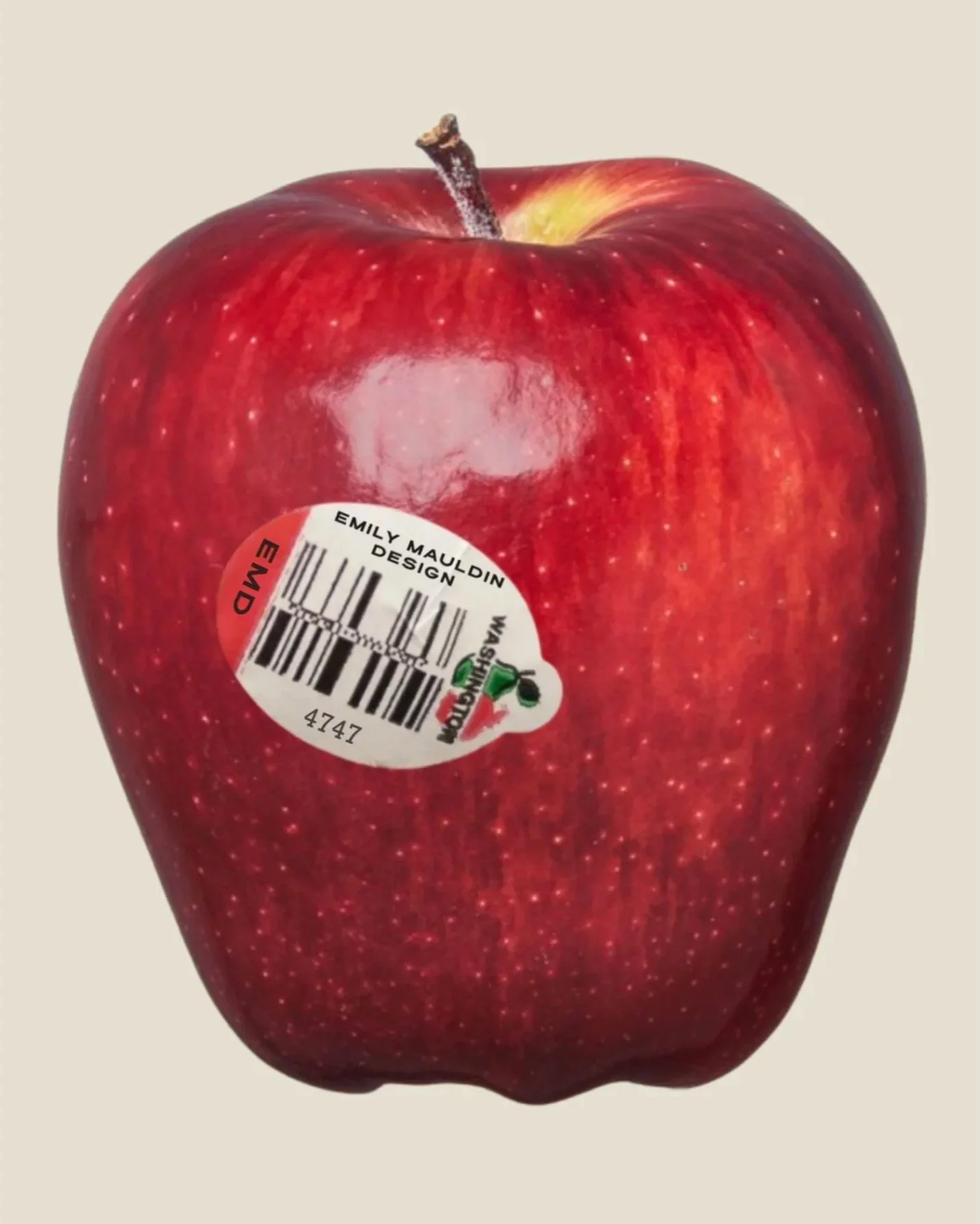 Fresh red apple with a sticker that reads 'Emily Mauldin Design' and includes a barcode.
