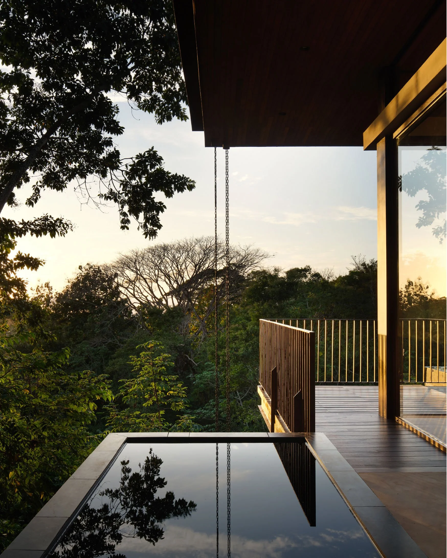 Minibauta House pool deck at dusk in Santa Teresa, Costa Rica, with timber decking and forest views, by FAMM Arquitectura
