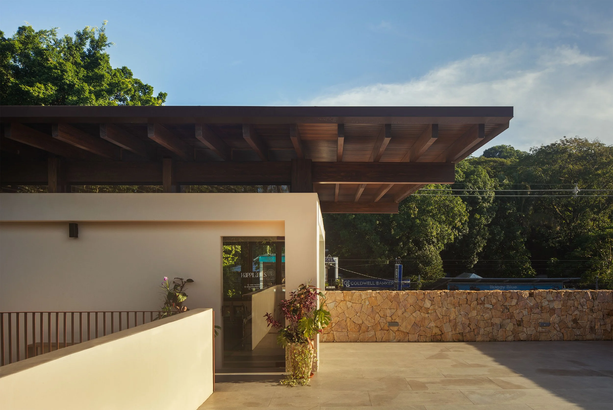 Plaza Pochote covered walkway with timber railing and stone wall in Santa Teresa, Costa Rica, by FAMM Arquitectura