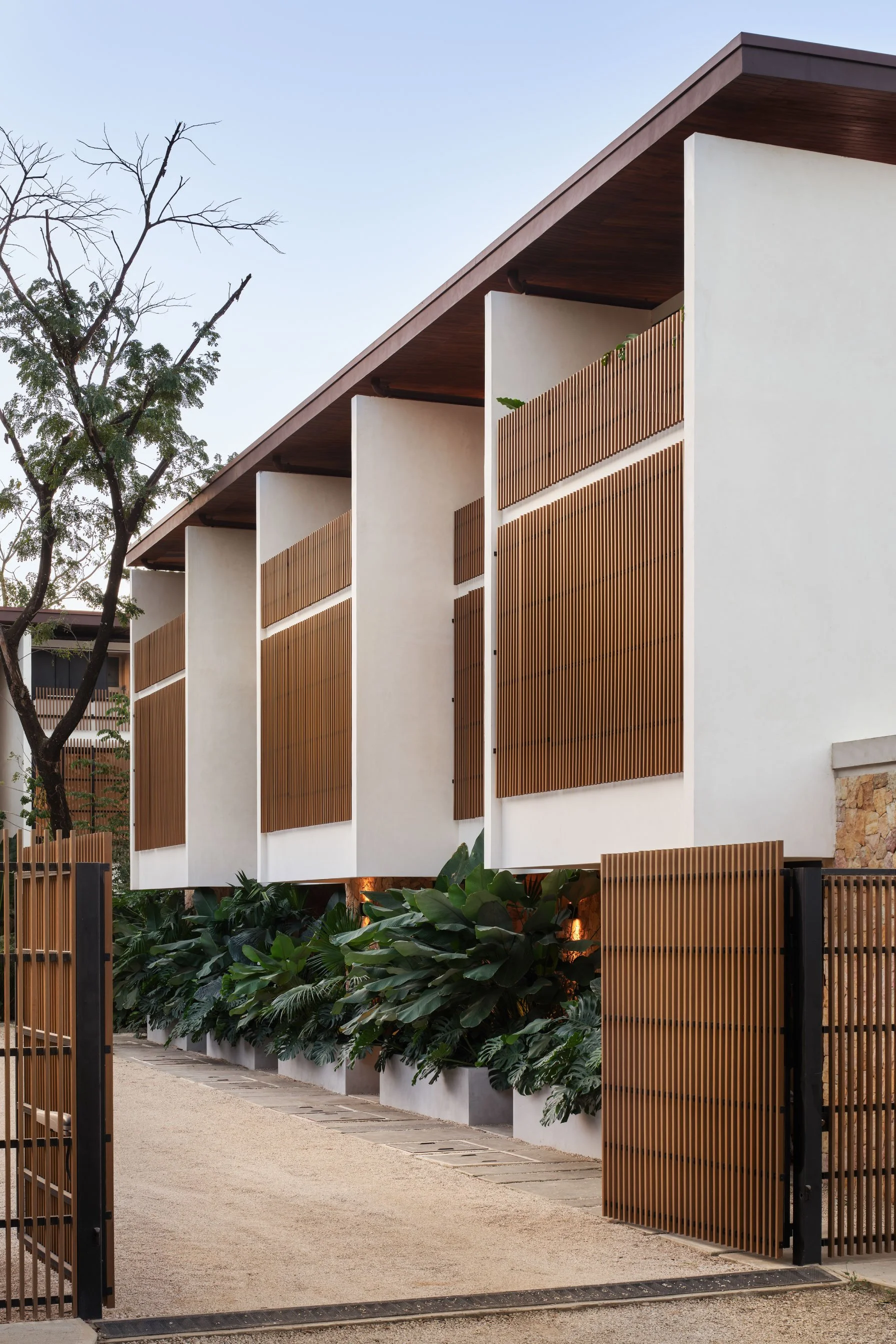 El Molino gated entrance in Nosara, Costa Rica, with timber louvers, stone walls and planters, by FAMM Arquitectura