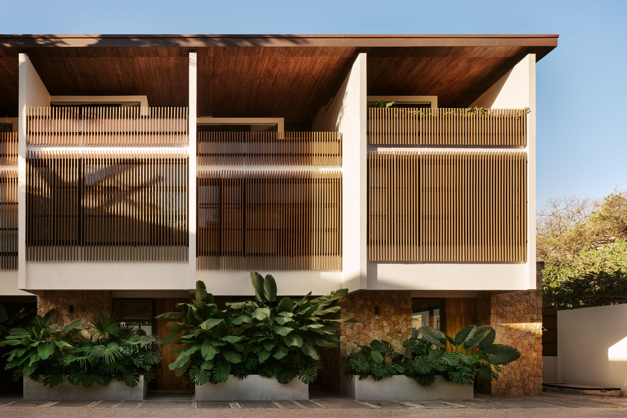 El Molino courtyard in Nosara, Costa Rica, with timber louvers, stone base and tropical planters, by FAMM Arquitectura