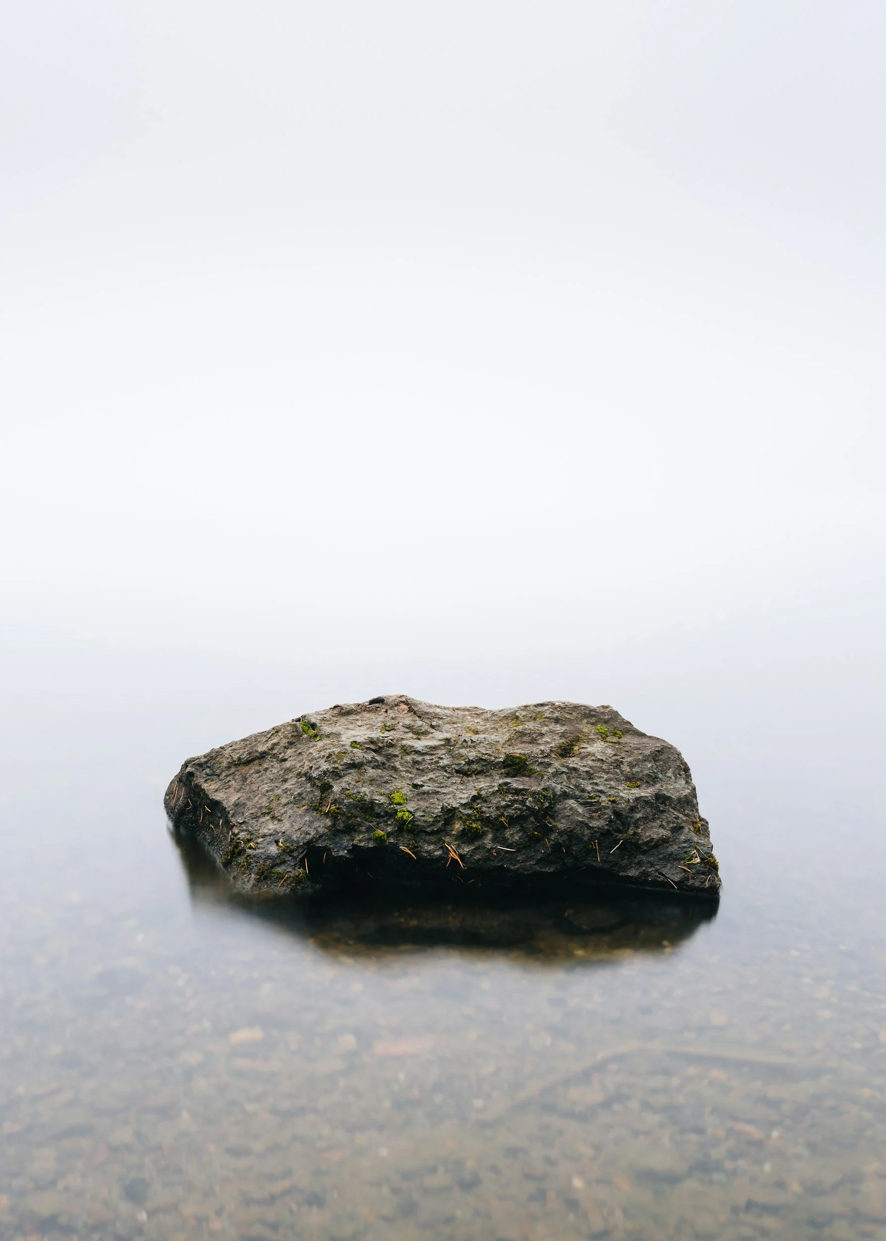 A single rock in calm water representing an individual connecting with themselves and their feelings.