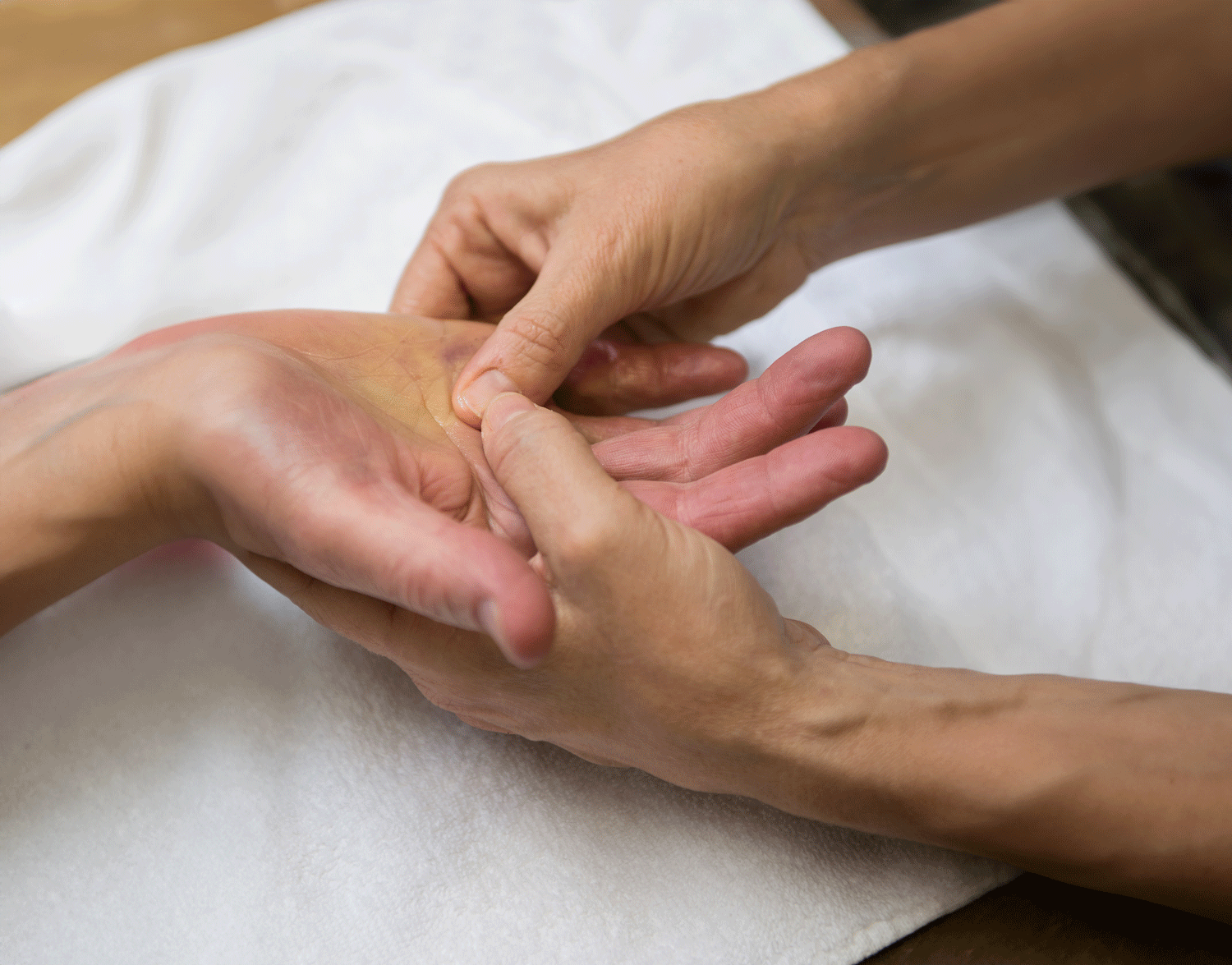 Two hands performing a massage or physical therapy on a person's hand, on a white cloth.