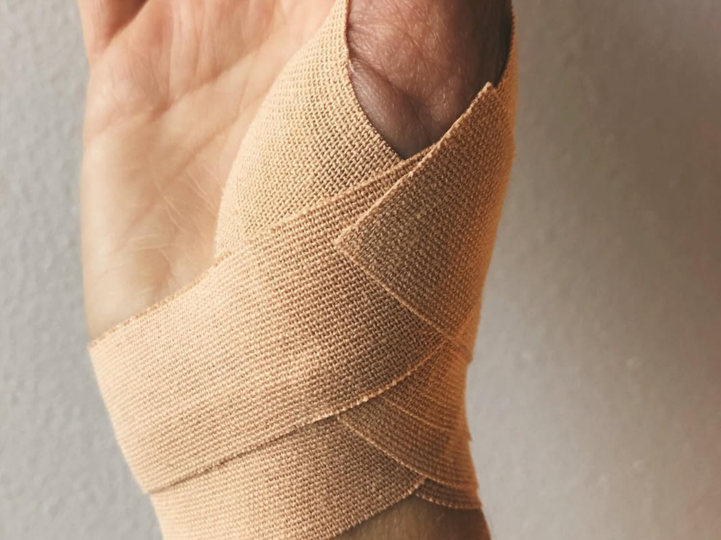 A hand with a bandaged thumb, with the bandage wrapped around the thumb and part of the wrist.