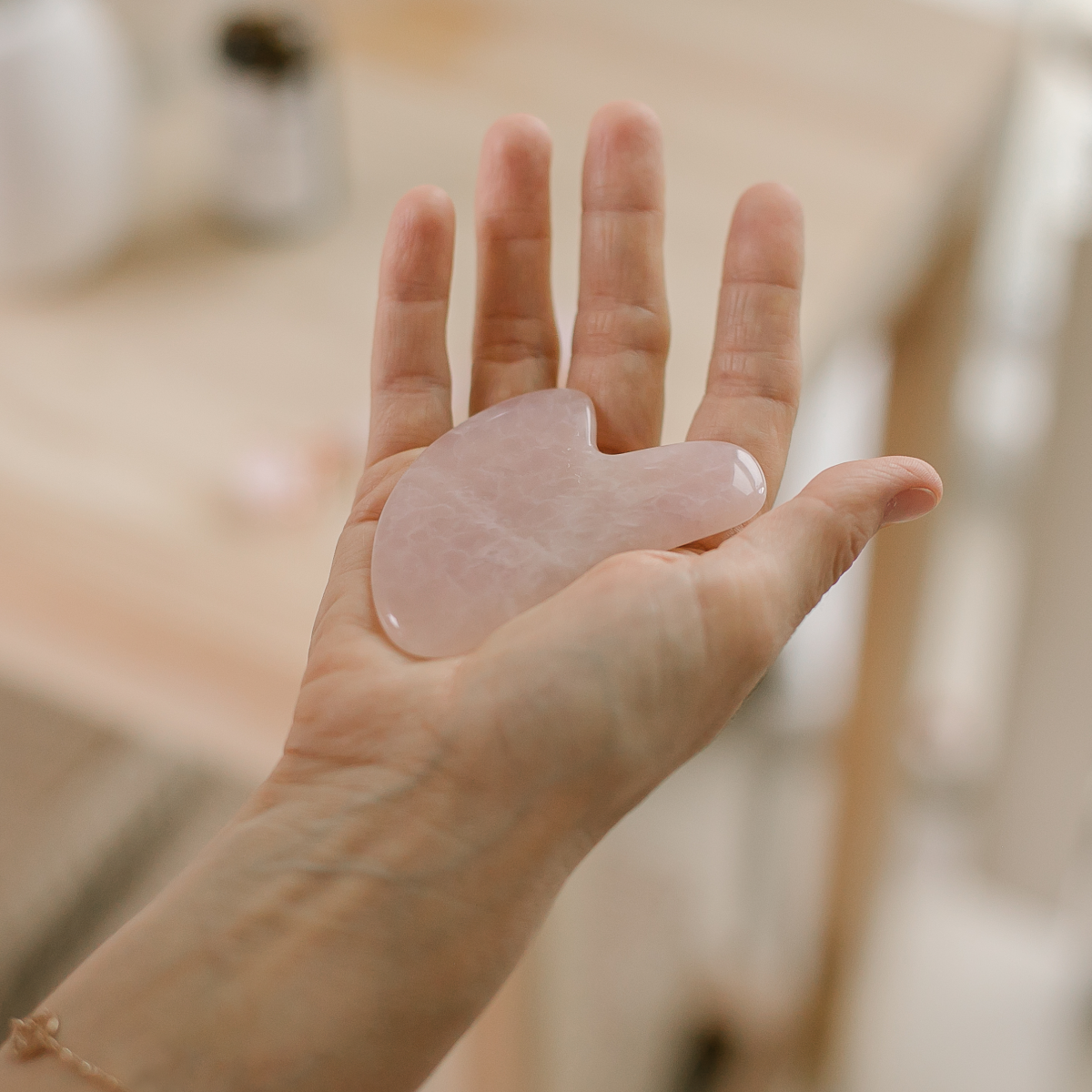 A hand holding a pink rose quartz Guasha stone.