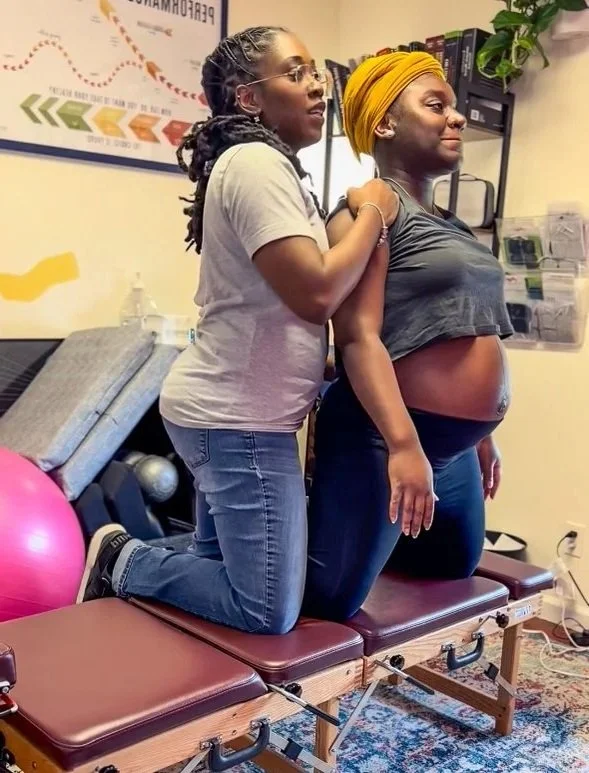 A pregnant woman receiving chiropractic care from Dr. Magen Henry in her office, with exercise equipment visible in the background.