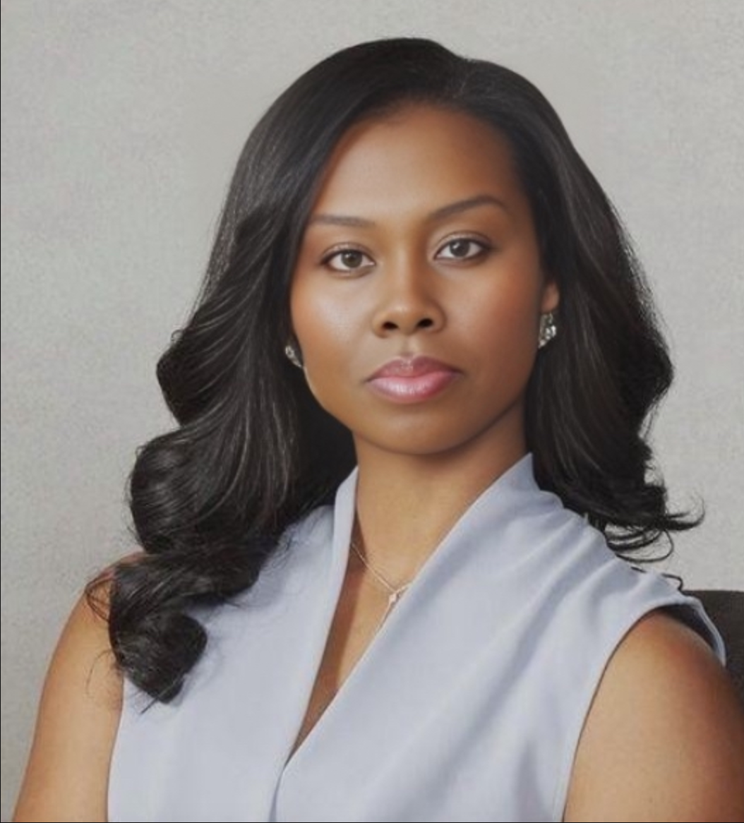 A woman with long black hair wearing a light blue sleeveless top, posing against a plain gray background.