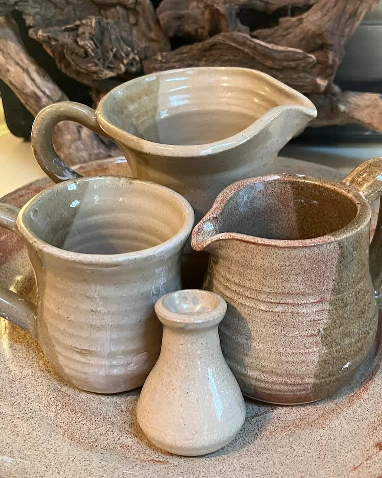 Collection of handmade ceramic mugs and pitchers on a wooden surface.