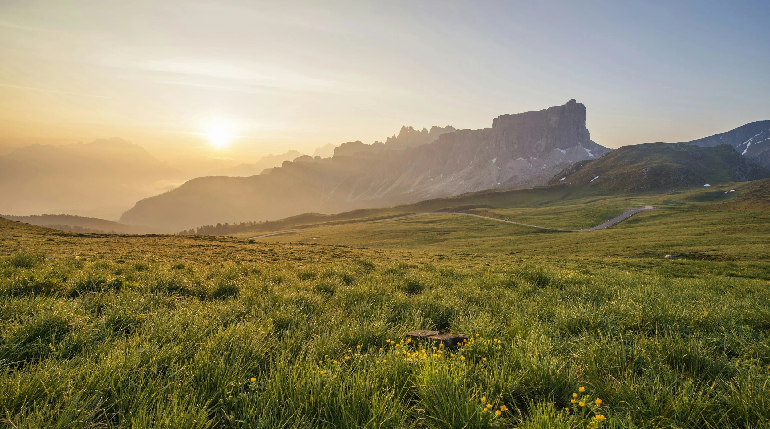 Sunrise over green grassy plains with mountains in the background and a clear sky.