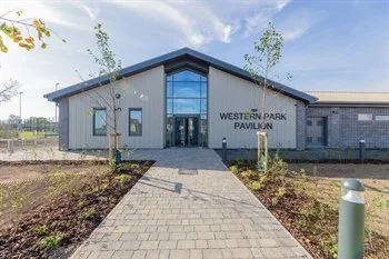A school playground with colorful fencing, trees with fall leaves, and a building with a mural, under a clear blue sky.