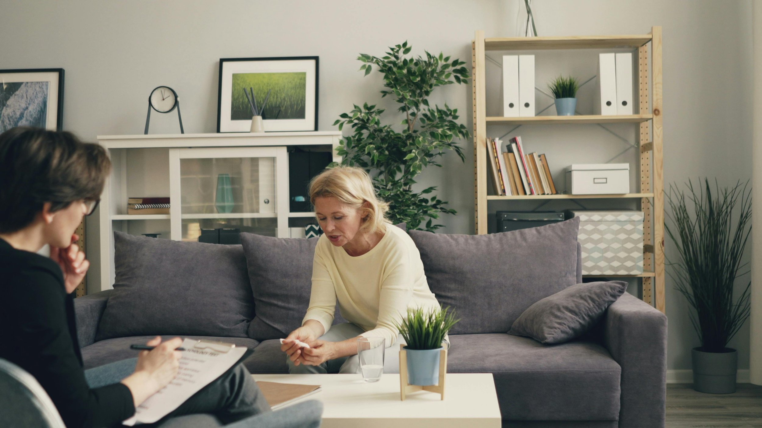 A depiction of a south jersey patient sitting on a dark gray couch with plants in the background and talking to a reproductive psychiatrist