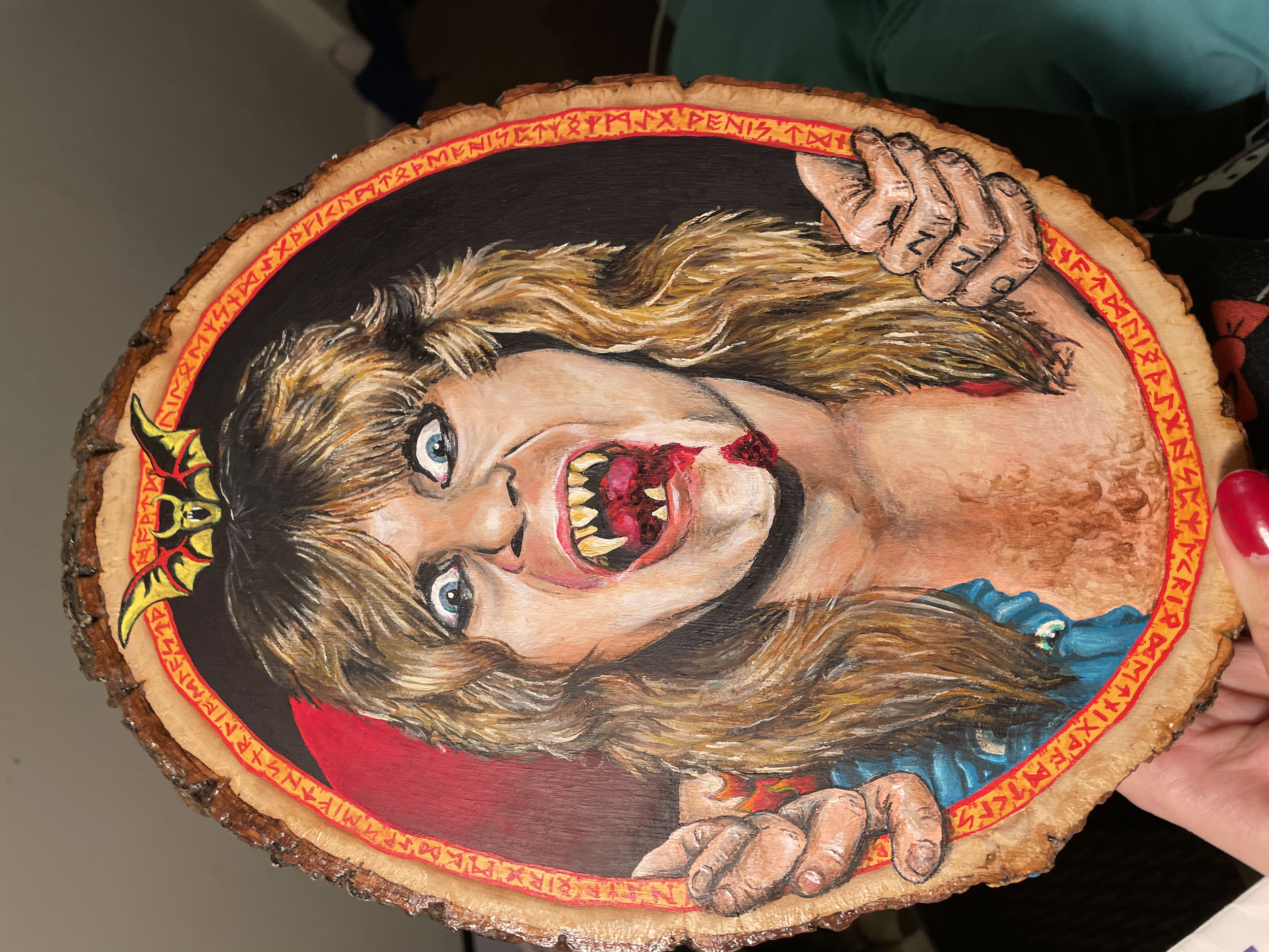 A large portrait of Ozzy Ozbourne painted in arcyllic on an oval-shaped slice of wood. The image is based on the Speak of the Devil album cover, in which the artist appears the be emerging fiercely from a red runic frame.