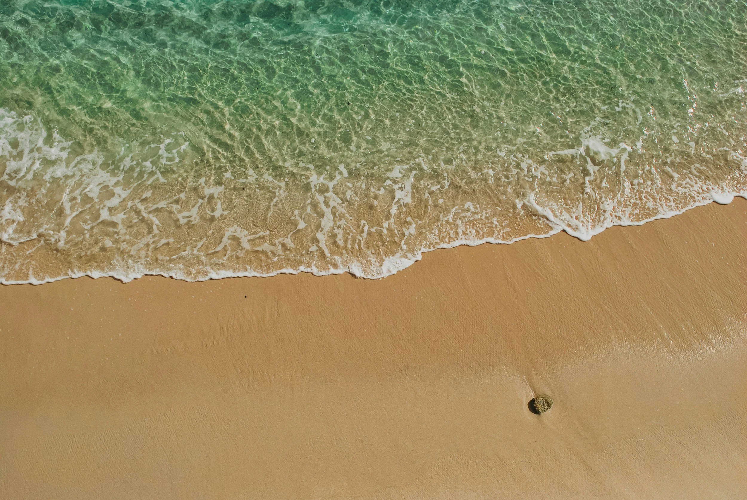 Beach with gentle waves and sand, small rock in lower right corner.