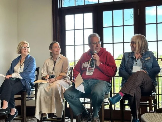 Four Barrington Area Development Council board members sitting on chairs near a large window, participating in a panel discussion. The person second from the right is speaking into a microphone, with others listening.