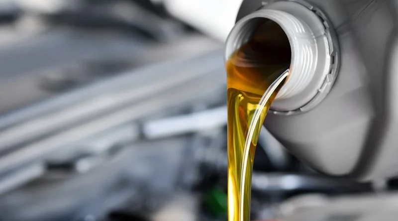 Motor oil pouring from a drain tube in a car engine compartment.