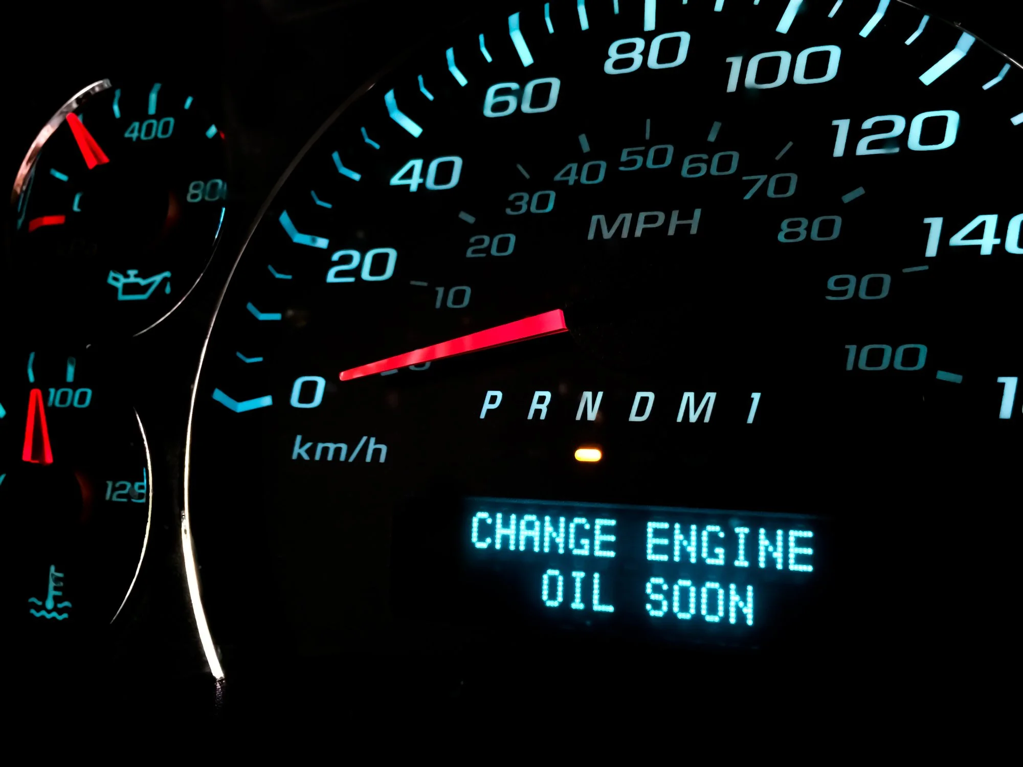Car dashboard showing the speedometer at 0 mph, oil change warning message, and other gauges.