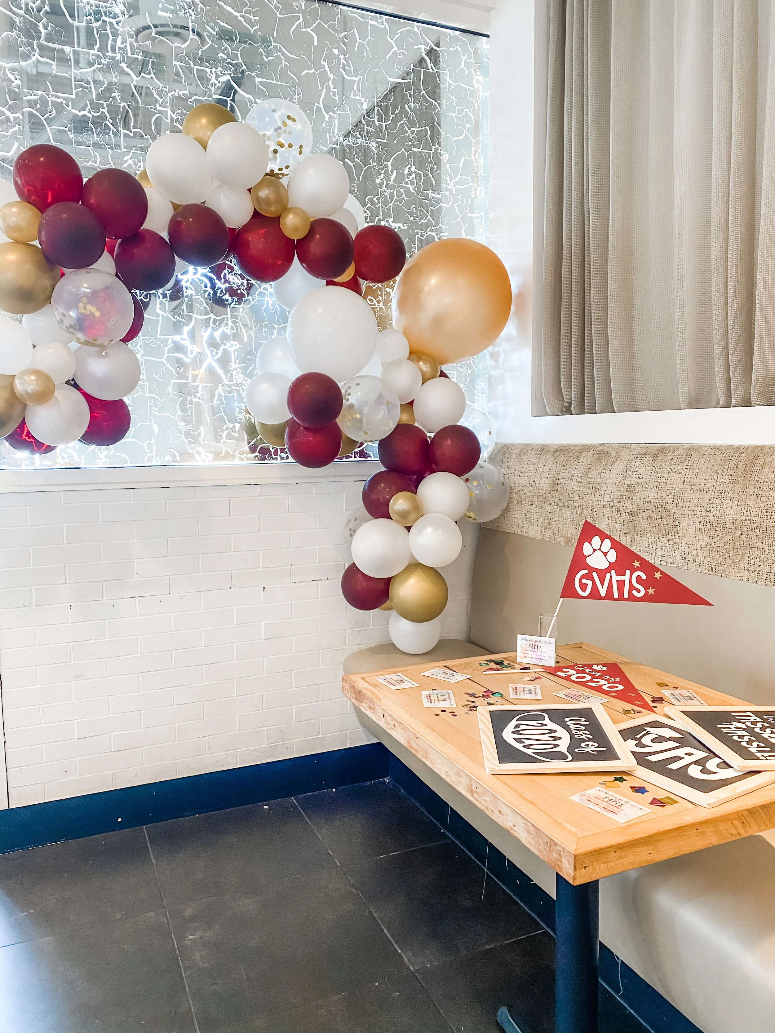 A corner of a room decorated with a colorful balloon arch and a table with celebratory signs related to graduation.